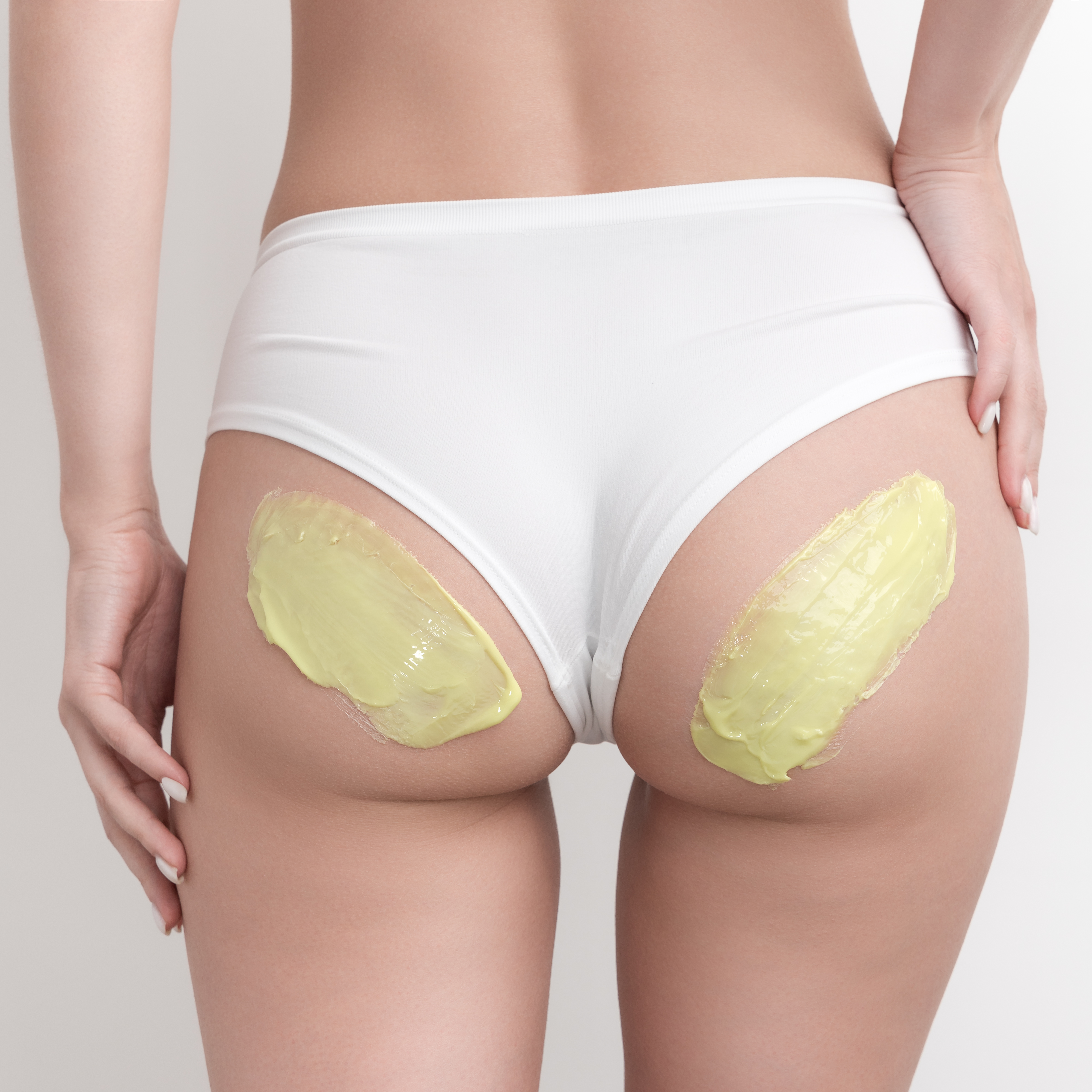 Green hot wax on woman buttocks. Healthy slim body in white panties during hair removal procedure