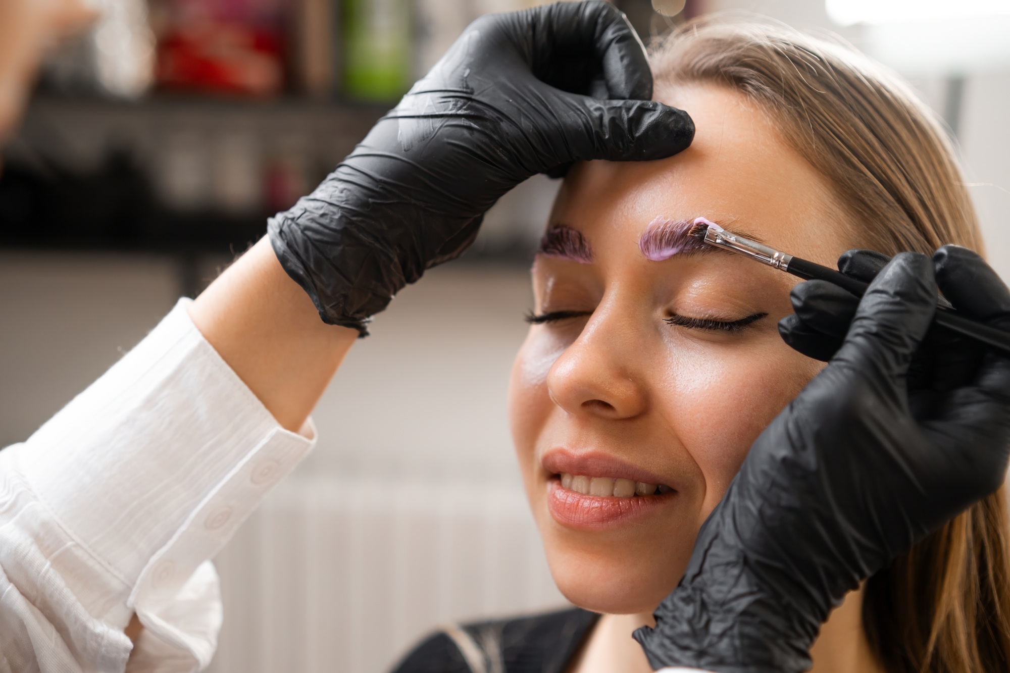 A woman is having her eyebrows laminated by a professional.