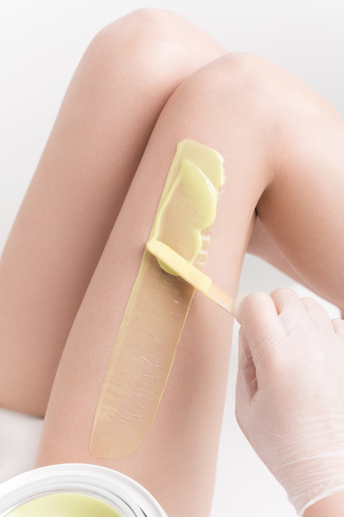 Applying hot wax on slim woman leg using spatula. Professional depilation, waxing in beauty salon